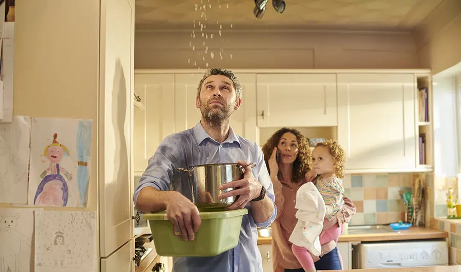 Family reacting to a ceiling leak while catching water in containers in Wilson, North Carolina.