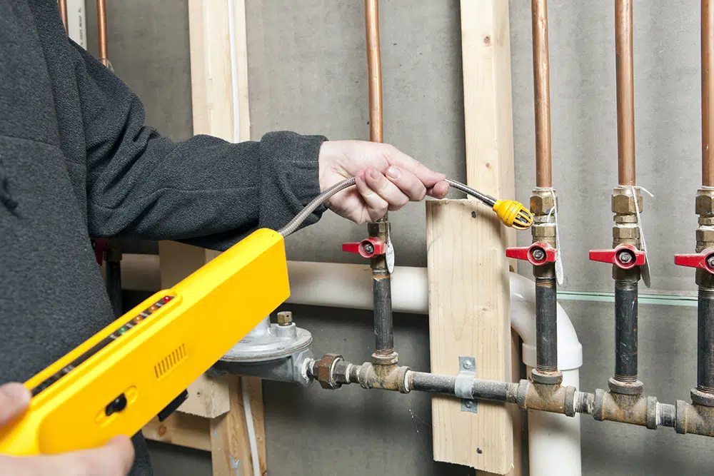Technician using a gas leak detector on exposed piping inside a home in the greater Wilson, NC region.