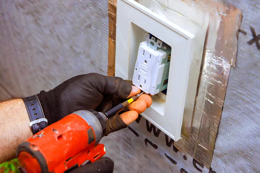 Electrician installing a GFCI outlet in a wall during a home upgrade near Wilson, North Carolina.