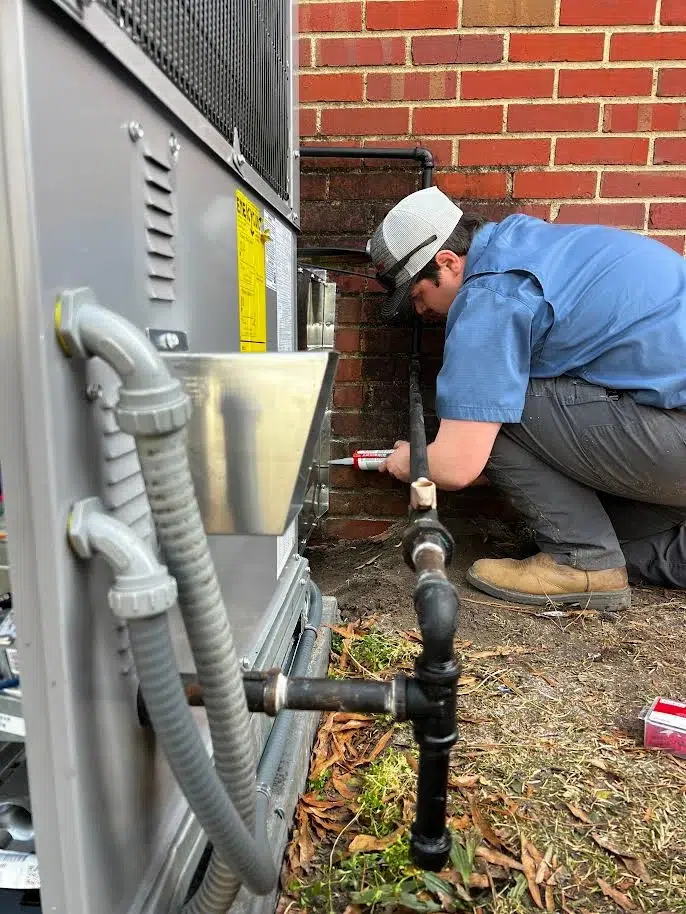 An HVAC technician working on an outdoor AC unit.