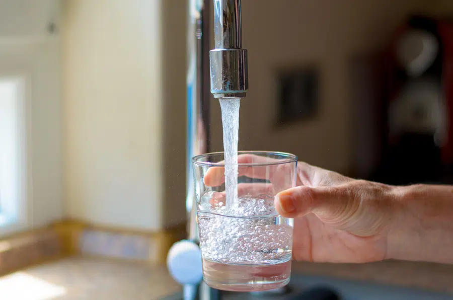 Hand filling a glass with clean drinking water from a kitchen faucet in the Wilson area.