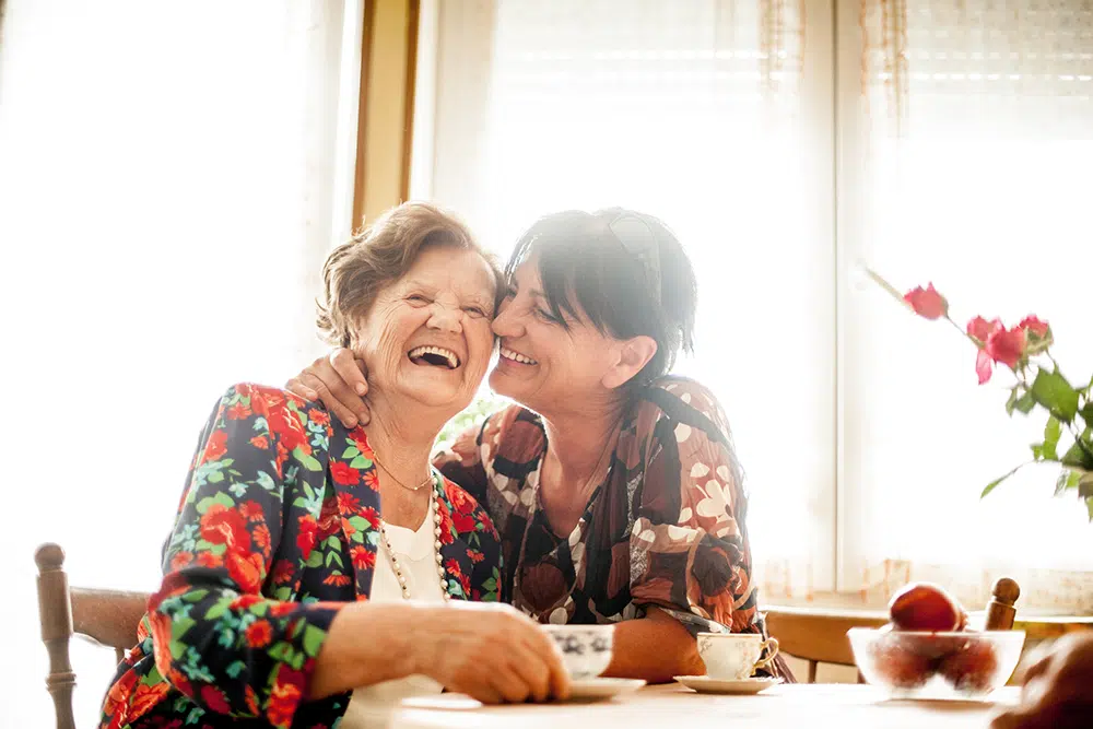 Two women sharing a happy moment at a kitchen table inside a home in Wilson, North Carolina.